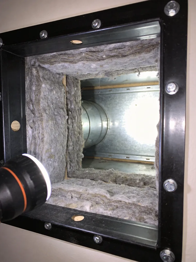Inside a residential air duct before cleaning, caked with dust and debris